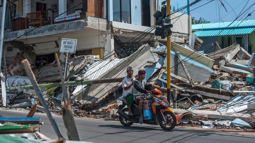 Motorists ride past buildings ruined by Sunday's earthquake in Pamenang.