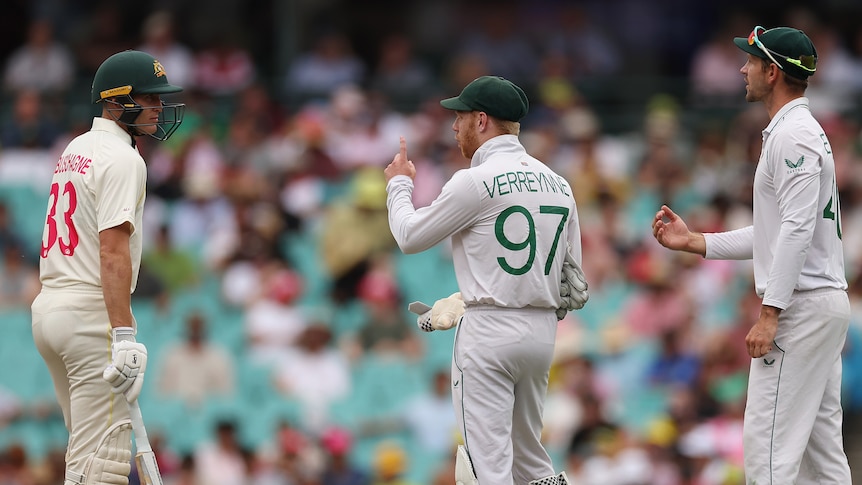Australia batter Marnus Labuschagne speaks to South Africa fielders during a Test. Kyle Verreynne is holding up his finger.