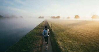 Mina Guli is seen running on narrow path at dawn, with paddock to right and river to left as sun rises and fog starts fading.