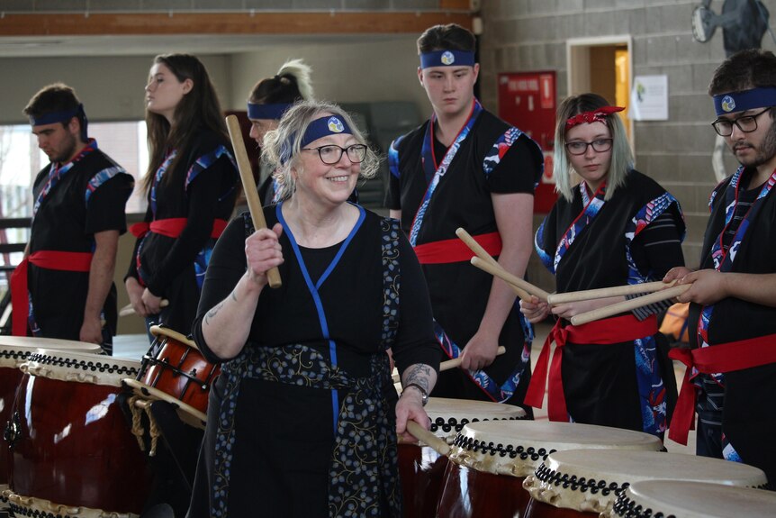 A teacher holding drum sticks, instructing students, who are dressed in traditional dress.