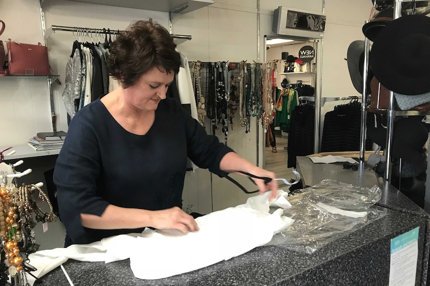 A woman folds clothes in a shop.