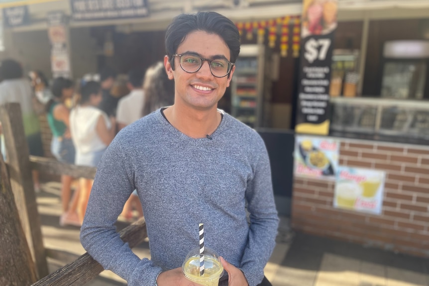 A young man of Indian decent holding a drink on the street