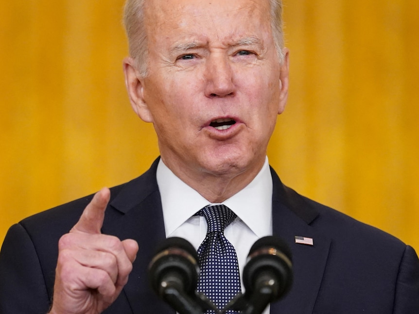 US President Joe Biden speaks from a podium in front of a yellow curtain, with one finger pointed