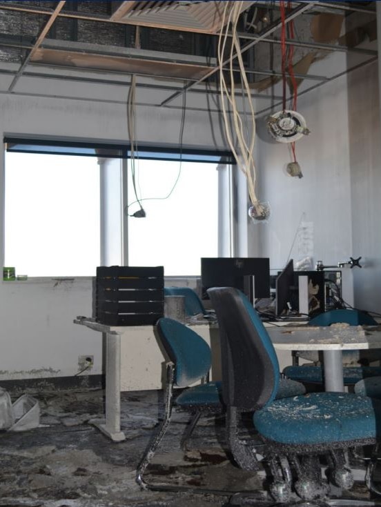 Wires hang down from the ceiling and debris litters the floor in an office within the prison.