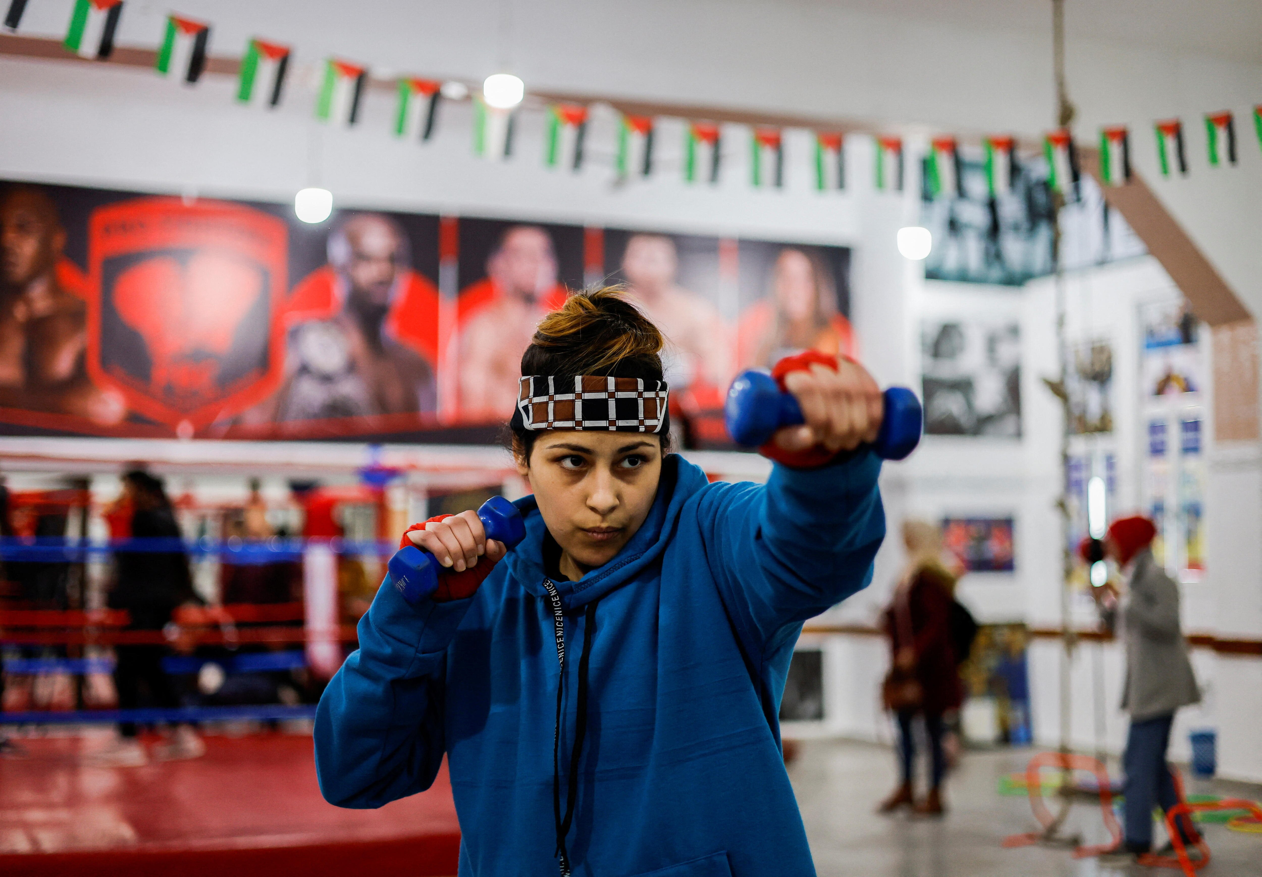 A girl holds weights up in a punching motion. 
