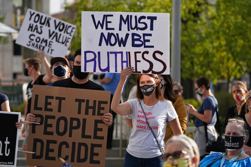 A woman holds a sign reading 'we must now be ruthless'