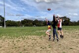 Three young boys try to mark a football.