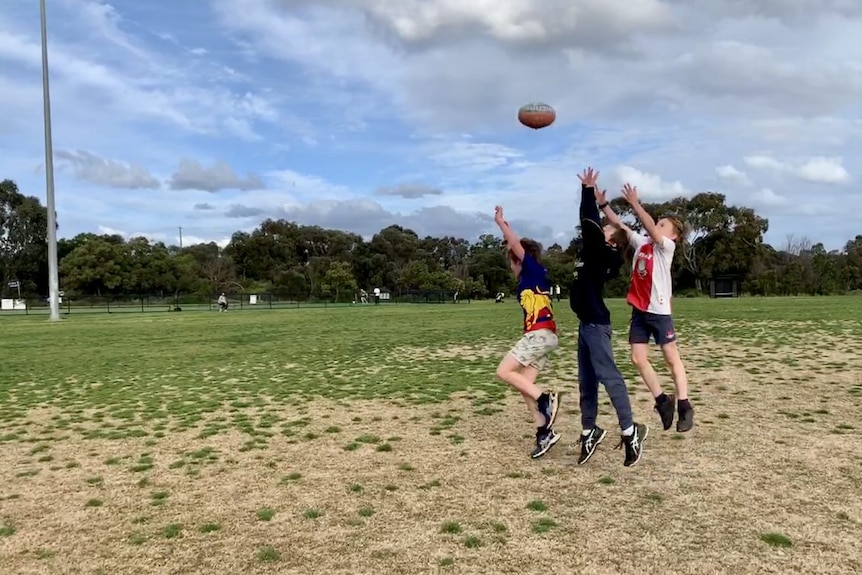 Three young boys try to mark a football.