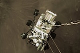 A white space vehicle is lowered to the ground above a dark, sandy planet.