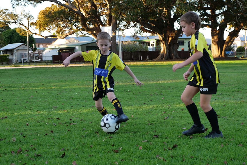 Two young boys wearing football uniforms kick a ball around on their local field. 