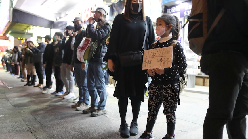 Young girl holds sign with Cantonese writing in protest.