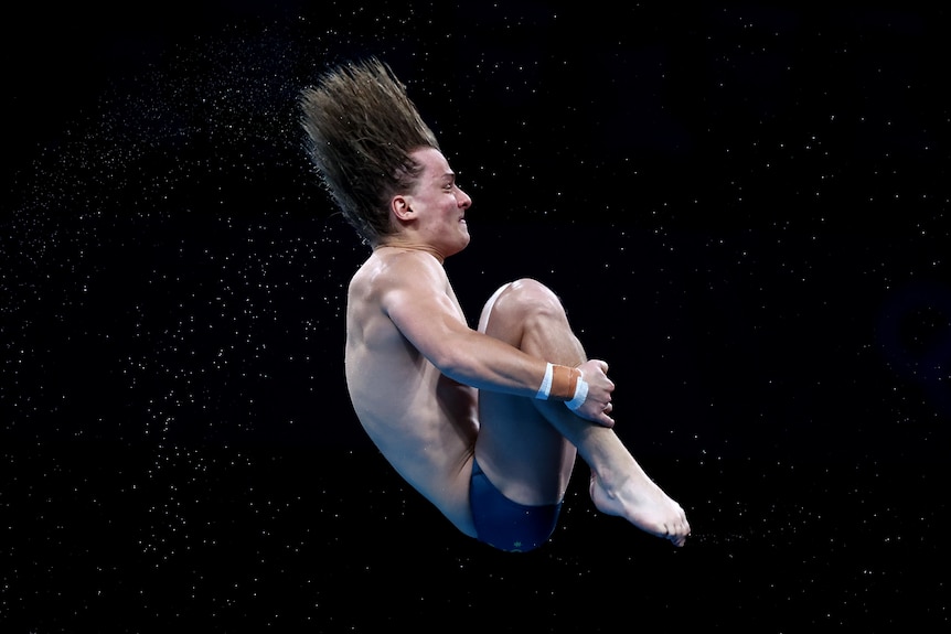 A man wearing blue speedos somersaults in the air