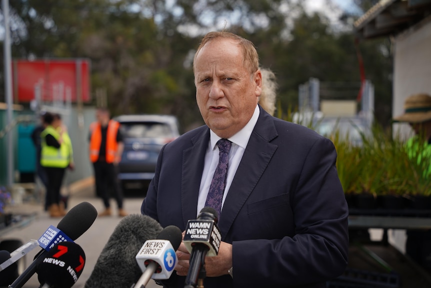 A man in a suit and tie speaks at a press conference. 