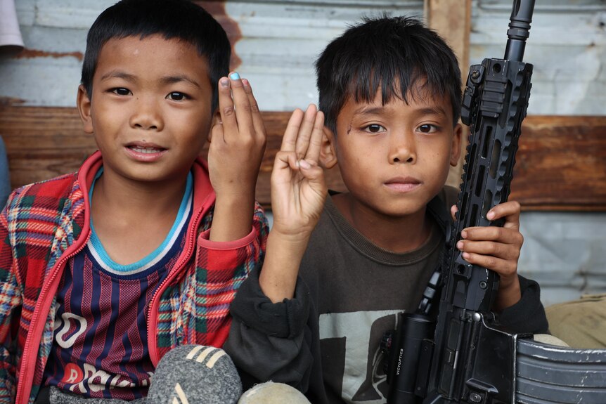 Two young boys smile at camera while holding a gun