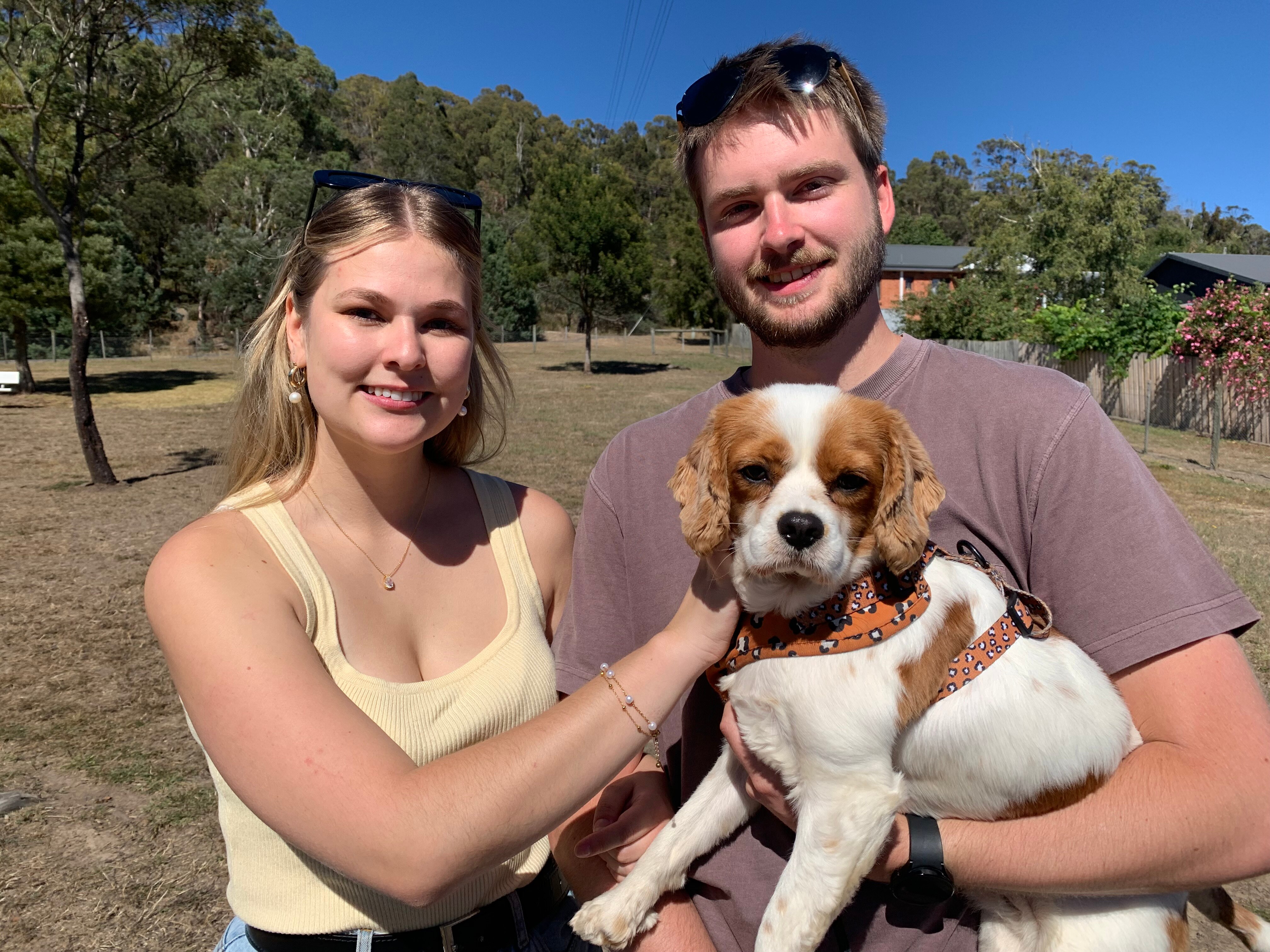 A young woman and man smile while holding a dog. 