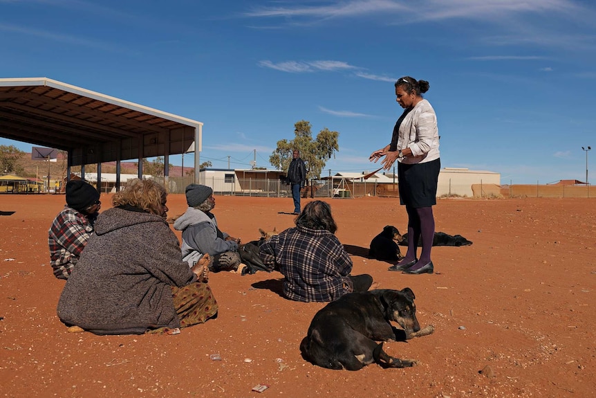 Leanne Liddle stands talking to four women on red dirt in an Aboriginal community.