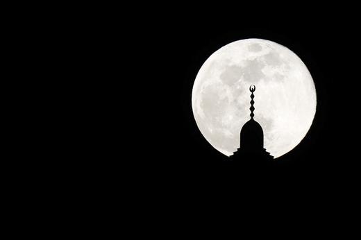 Bright full moon in background, mosque spire silhouetted in foreground