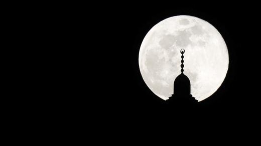 Bright full moon in background, mosque spire silhouetted in foreground