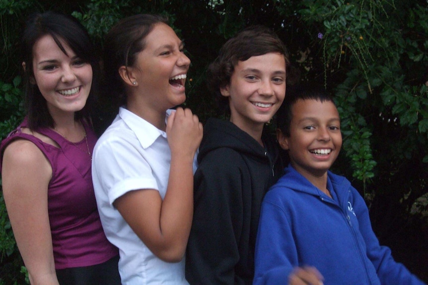 Four young people lined up in front of a hedge.