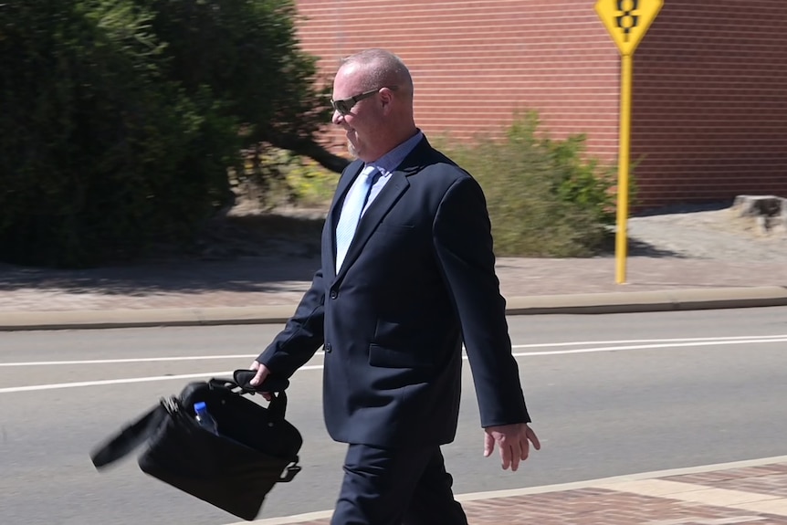 Man in a suit holding a laptop bag and walking on the street. 
