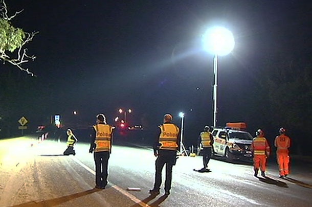 Police investigators standing around at the scene of the crash which is illuminated by a bright light.