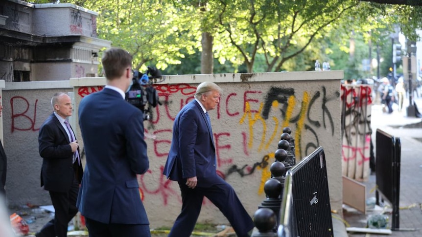 Donald Trump walks past graffiti outside