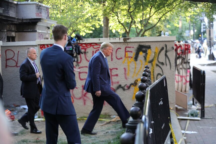Donald Trump walks past graffiti outside