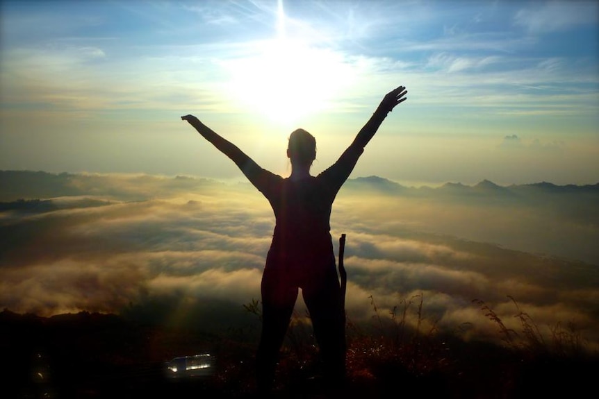 A girl stands above the clouds looking at a volcano in indonesia