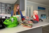 mother unpacking shopping in kitchen with toddler on bench