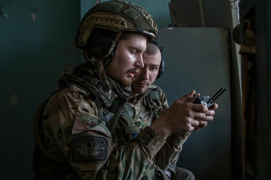 Two soldiers look at a drone controller.