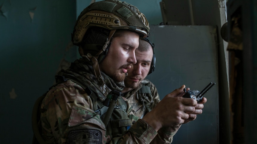 Two soldiers look at a drone controller.