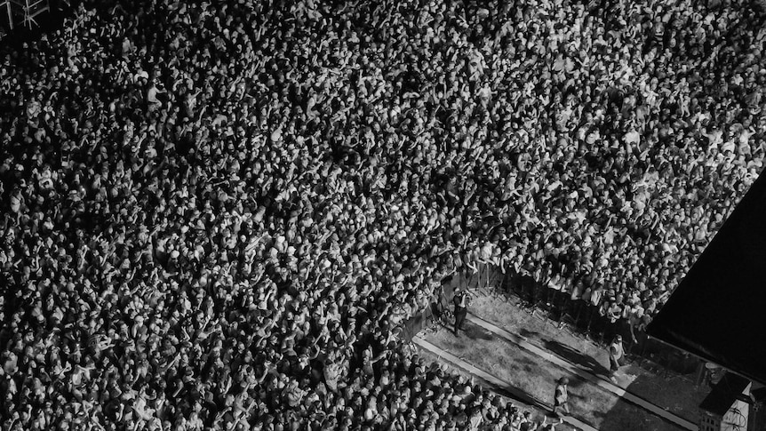 Black and white aerial photo of a large concert crowd with a single photographer in a cut out section.