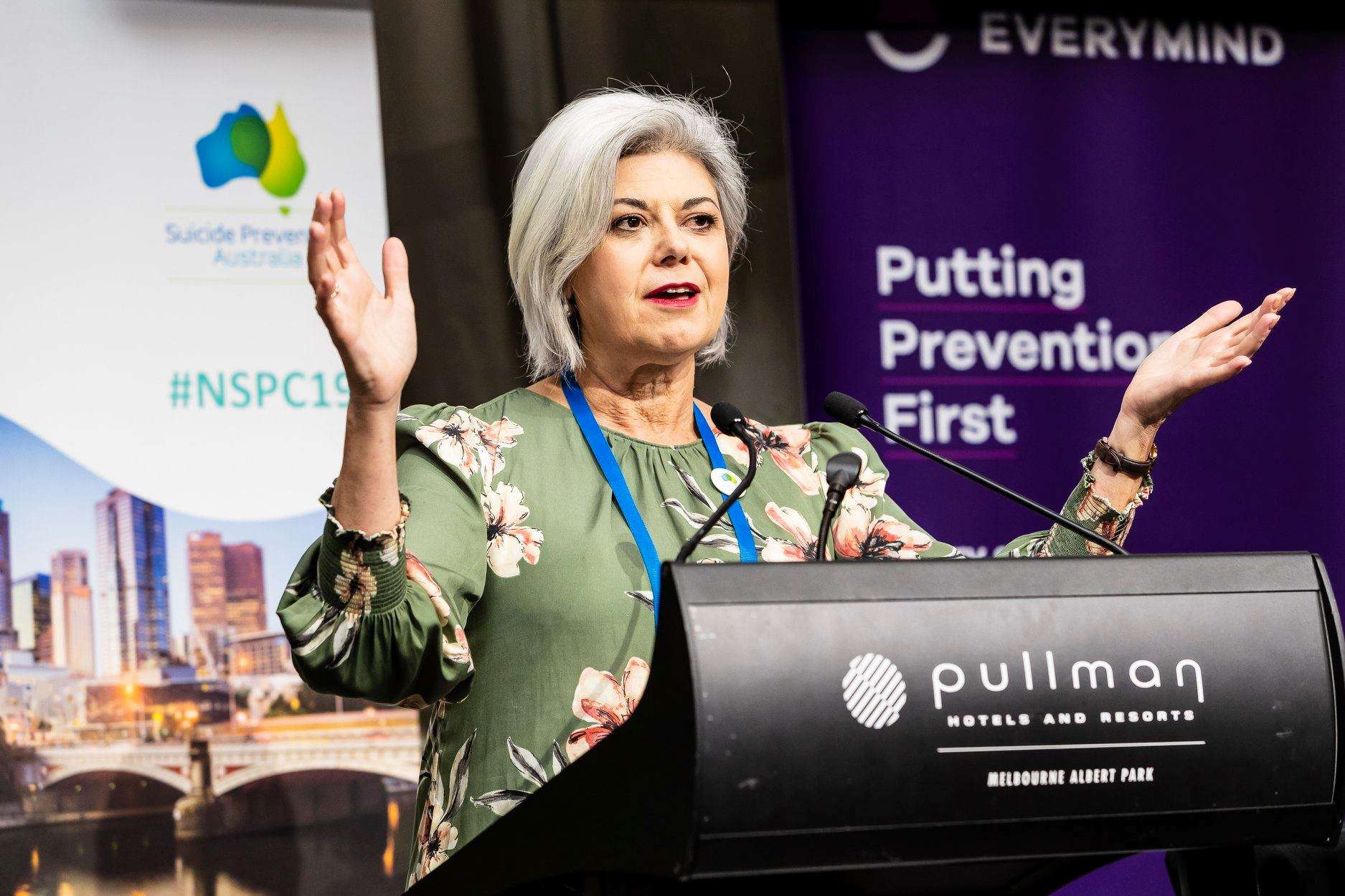 A lady speaks into microphones with her hands raised.