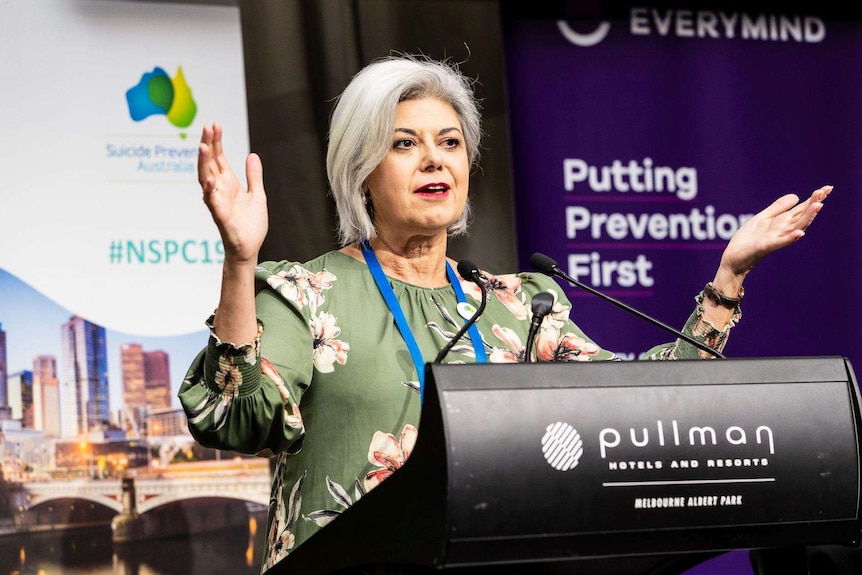 A lady speaks into microphones with her hands raised.