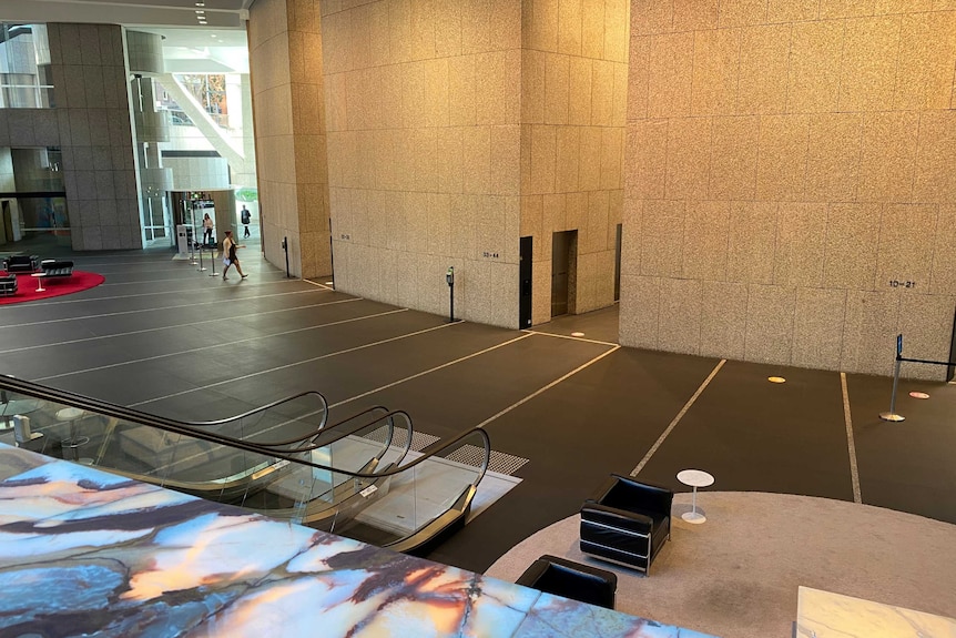 A large empty lobby with a grey concrete floor and walls and two still escalators.