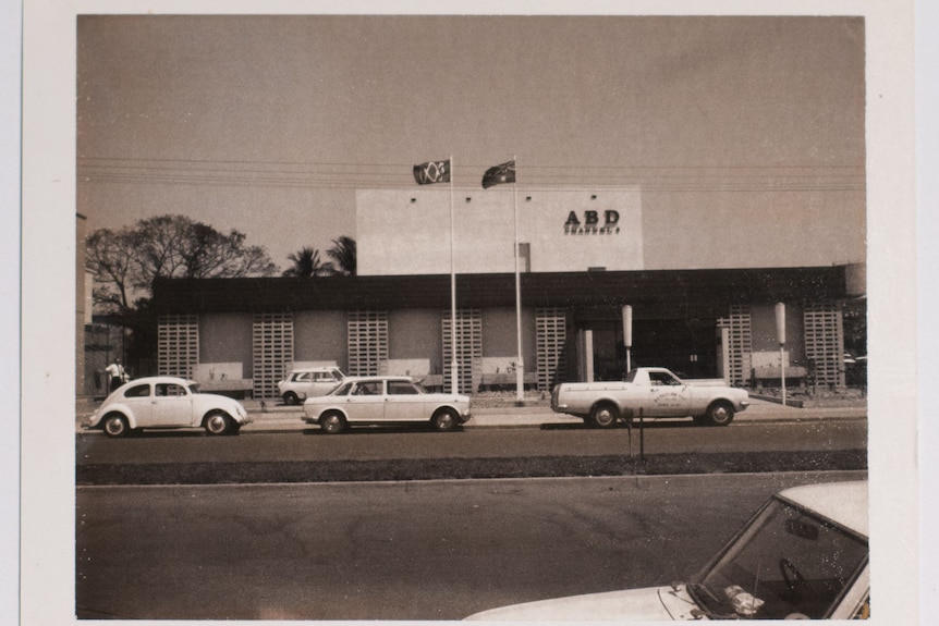 A black-and-white photo of the old ABC studios in Darwin. Retro cars are parked out the front.