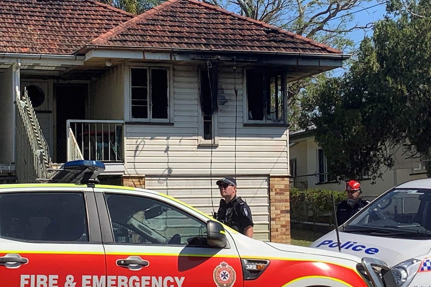 A policeman and emergency vehicles outside a house gutted by fire