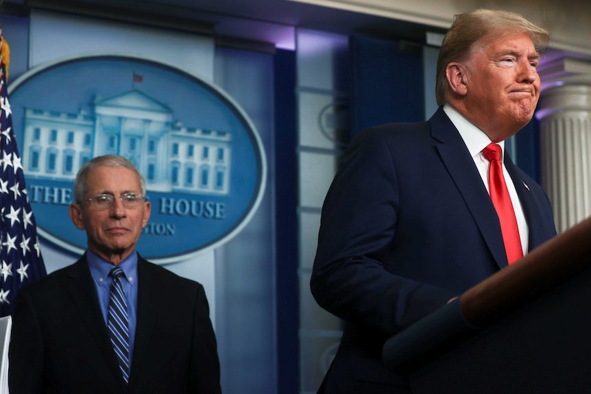 Donald Trump at a lectern while advisor Anthony Fauci looks on