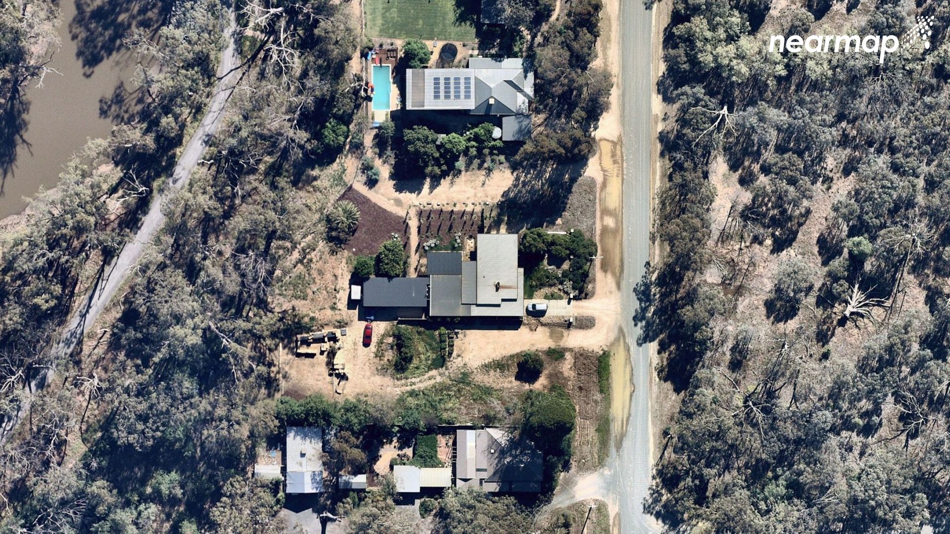 Three homes can be seen next to a river, with bushland opposite the houses