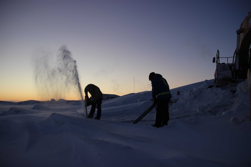 Two people hack into the sea ice in Antarctica with only a little sunlight to aid them.