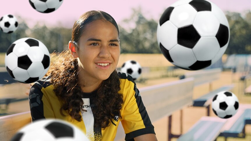 Melanie sits on a bench on the edge of a soccer field talking to a reporter off camera. Seven soccer ball icons float around.