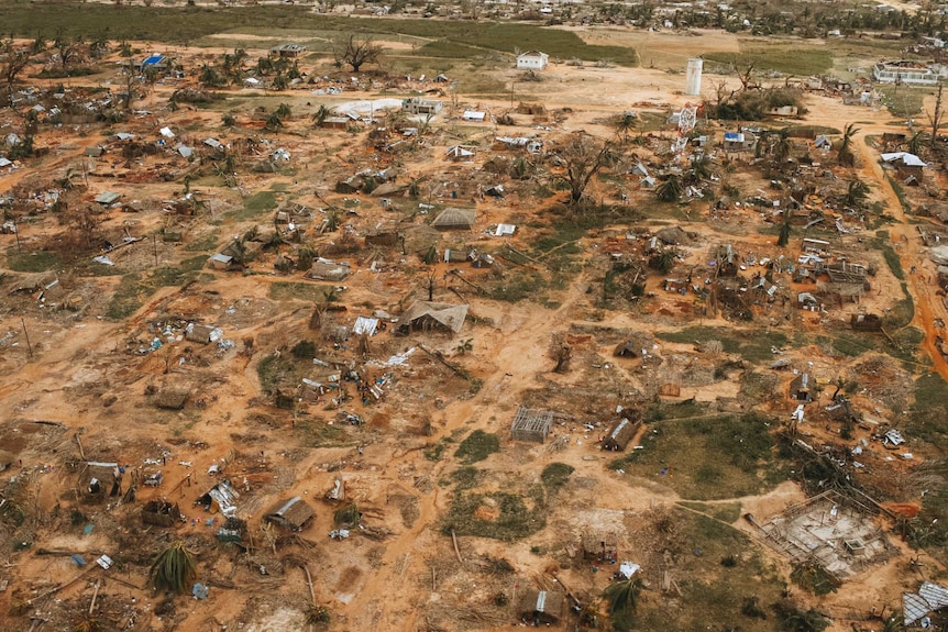 A shanty town in Mozambique that has been flattened by a cyclone, with housing materials and trees strewn across orange dirt.