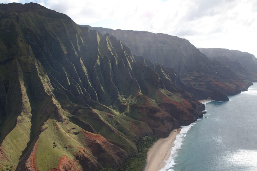 Towering green cliffs tumble down to the coastline in this drone shot of Kauai