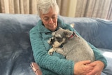Lyn Read is sitting, wearing an aqua green jumper. With her dog between her arms.
