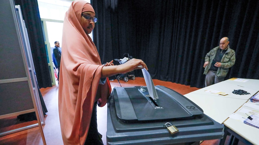 A woman wearing a headscarf places her vote in a ballot box