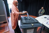 A woman wearing a headscarf places her vote in a ballot box