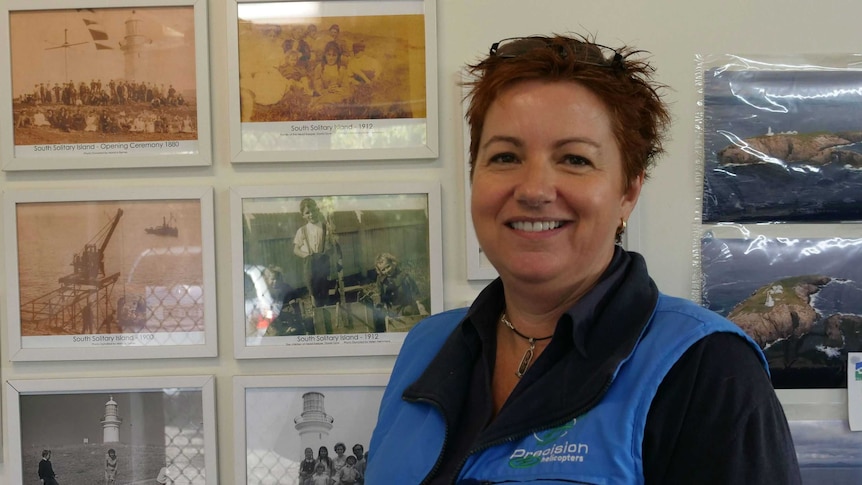 A woman stands smiling in front of a series of historic black and white photos pinned to the wall.