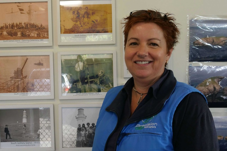 A woman stands smiling in front of a series of historic black and white photos pinned to the wall.