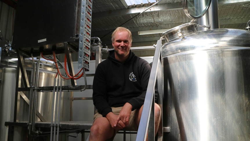 a brewer sits in between tanks of beer