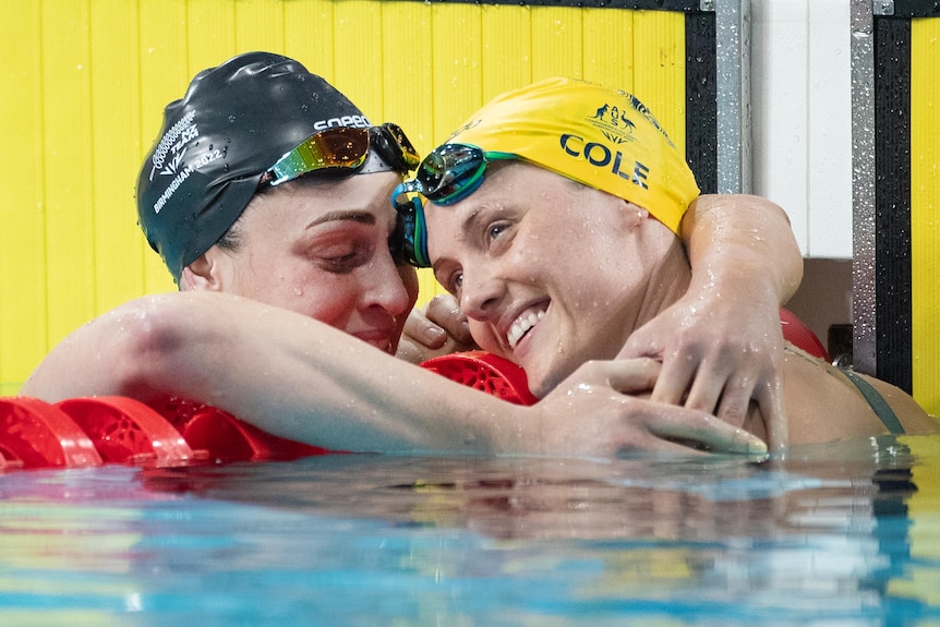 Ellie Cole is hugged by Sophie Pascoe. They are at the end of a pool. 